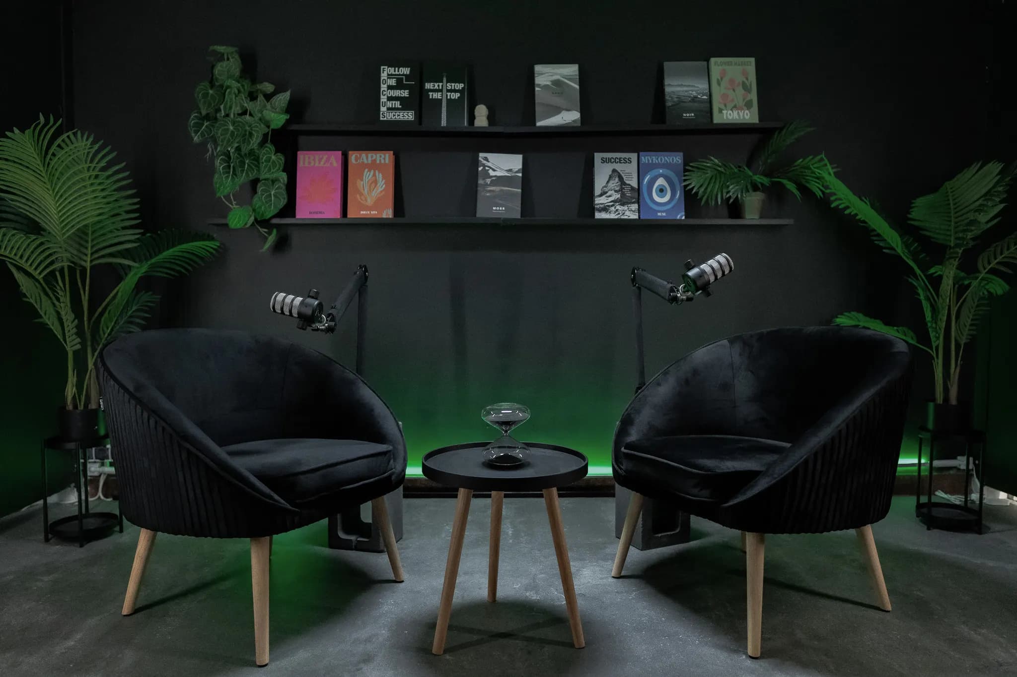 Noir Lounge: két fekete kagylófotel zöld háttérfényben, könyvespolc, pálmák