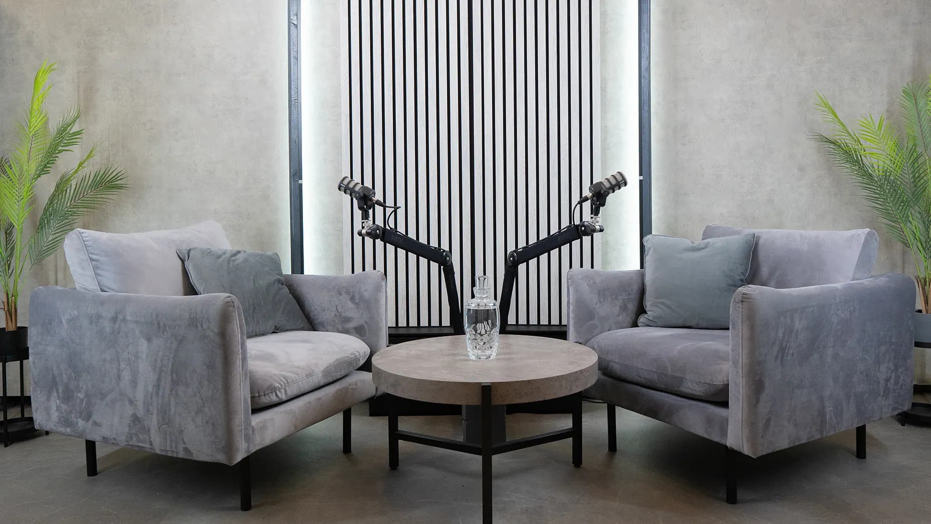 Steel Loft: két szürke bársonyfotel mikrofonokkal, kerek asztal kristálykancsóval, világító lamellás fal